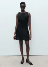 Vestido corto negro de corte evasé, confeccionado en mezcla de lino y lyocell. Presenta cuello barco, sin mangas con tirantes anchos, y detalle de pliegues en la falda. Cuenta con cierre de cremallera en la parte posterior.