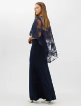 Vestido largo de corte sirena en color azul marino, confeccionado en tejido de punto con caída fluida. Presenta una capa integrada de tul fino sobre los hombros y espalda, decorada con bordados florales a tono y lentejuelas brillantes. Posee escote redondo y cierre invisible en la espalda.