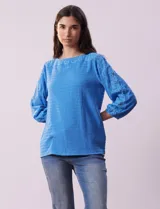 Blusa celeste texturada con escote redondo y mangas 3/4 con puño elastizado y aplique de broderie.