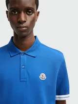 Polo azul de algodón piqué con cuello clásico, tapeta de dos botones y mangas cortas con ribete blanco. Parche con logo de Moncler en el pecho.