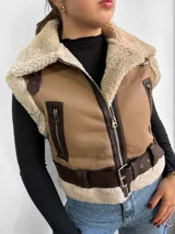 Chaleco color beige con interior de piel sintética color crema, cierre frontal con cremallera, bolsillos laterales con cremallera, cuello con solapas y cinturón ajustable en la cintura.