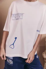 Remerón de corte oversize color off-white, con cuello redondo y mangas cortas. Presenta estampados en color azul que incluyen un dibujo de un edificio, una llave con forma de corazón y la palabra 'renée'.