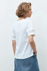 Remera blanca de algodón con cuello en V y mangas cortas que presentan un detalle de puntilla en los bordes.