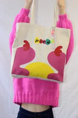 Tote bag de lienzo color crudo con estampado de diseño abstracto en colores rosa, amarillo y rojo. Incluye charm colgante con cuentas de colores.