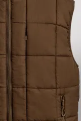 Chaleco marrón acolchado con cuello alto, cierre frontal con cremallera, bolsillos laterales con cremallera y bajo ajustable con trabilla y cremallera lateral.