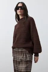 Sweater de punto color marrón chocolate, con cuello redondo, mangas largas abullonadas y puños ajustados. Presenta un diseño de textura acanalada horizontal y silueta relajada.