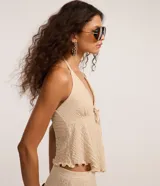 Blusa beige texturizada de corte halter con escote en V, lazo frontal ajustable en el busto y ruedo asimétrico ondulado.