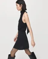 Vestido corto negro sin mangas con cuello alto drapeado y lazo en la parte posterior.