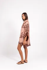 Vestido corto de silueta amplia, color tostado con bordados barrocos en contraste, escote en V con botones de madera, mangas anchas tipo capa con flecos de cuentas en los bordes.