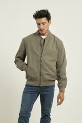 Campera tipo bomber color verde militar, confeccionada en 100% algodón. Cuenta con puños tejidos al tono, cuello y cintura elásticos, y cierre frontal metálico.