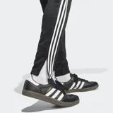 Pantalón de jogging negro Adidas Tiro 25 Essentials con tres rayas blancas en los laterales, corte ajustado y bolsillos con cierre.