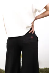 Pantalón de lino blanco de corte amplio y tiro medio-bajo. Presenta bolsillos laterales y traseros, cierre con botón metálico y detalles bordados sutiles en los laterales y la parte trasera.