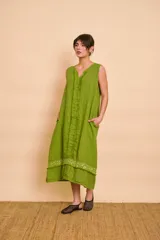 Vestido midi verde sin mangas, de corte holgado, escote en V y bolsillos laterales. Cuenta con detalles de aplicaciones bordadas con lentejuelas en el ruedo y una franja vertical con flecos en el centro del frente.