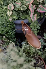 Zapatos tipo chelsea de cuero color marrón, con paneles elásticos laterales y suela plana de goma.