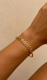 Brazalete rígido de acero dorado con una fila central de dijes de estrellas huecas conectadas entre sí.