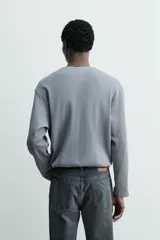 Camiseta relaxed fit de manga larga confeccionada en tejido waffle con mezcla de algodón y cáñamo. Presenta cuello redondo con cierre frontal parcial de botones.