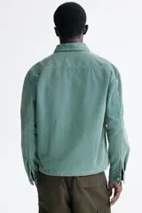 Sobrecamisa de pana de algodón color verde, con cuello clásico, cierre frontal de cremallera, mangas largas con puños abotonados y bolsillos superiores con solapa y botón.
