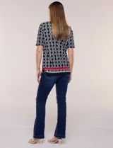Remera de algodón con estampado geométrico en blanco y negro, de manga corta, con detalle de guarda roja y flecos en el ruedo.