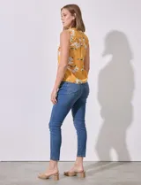 Blusa amarilla sin mangas de satén estampado con flores blancas. Tiene cuello a la base y escote en V.