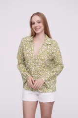 Blusa de algodón con estampado de hojas en tonos verdes sobre fondo blanco, cuello camisero, cierre frontal con botones y mangas largas.