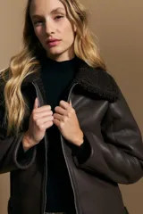 Campera tipo gamulán de cuero sintético negro, con interior y detalles de corderito sintético al tono en cuello y ruedo. Presenta cierre frontal metálico y diseño de silueta relajada.