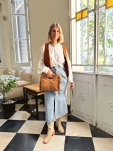 Cartera bandolera de cuero color camel, con forro interno de tela y flecos laterales.