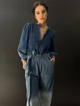 Mono largo de jean azul con lavado artesanal, escote en V regulable con cierre invisible, mangas largas abullonadas y lazo en la cintura.