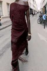 Vestido midi asimétrico de un solo hombro en color bordó, confeccionado en tejido devoré con diseño floral y detalles de terciopelo. Presenta frunces laterales, bajo con flecos largos y aplicación de tachas metálicas. Incluye forro interior y cierre lateral con cremallera oculta.