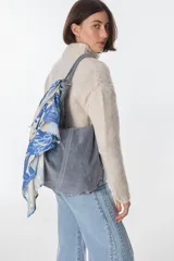 Bolso tipo tote de cuero color gris con costuras verticales al frente y pañuelo estampado atado a la correa.