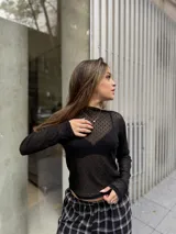 Polera de manga larga confeccionada en tela de encaje negro con textura geométrica. Presenta un diseño ajustado al cuerpo con cuello alto y acabado semitransparente.