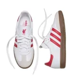 Championes Adidas modelo Samba, de diseño clásico con base de cuero blanco, franjas laterales rojas, puntera de gamuza gris y suela de goma color caramelo.