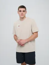 Remera de manga corta color beige, con cuello redondo y diseño holgado. Cuenta con un pequeño estampado rectangular en el pecho con motivo futbolero.