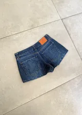 Short de jean azul de tiro bajo, con bolsillos traseros appliqués que presentan un diseño de estrella acolchada. Incluye etiqueta de cuero sintético naranja en la parte posterior de la cintura.