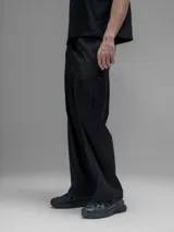 Pantalón cargo negro de corte oversize, confeccionado en microfibra elastizada. Presenta cintura elástica, bolsillos laterales y un bolsillo cargo con cierre de broche a presión. Incluye un sistema de elásticos con tancas en los tobillos para ajustar la apertura.