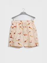 Bermudas de algodón color crema con estampado de sirenas en tonos naranja y marrón. Tiene cintura elástica con cordón ajustable, dos bolsillos laterales y un bolsillo trasero.