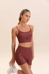 Top deportivo color ladrillo, de impacto medio, con escote redondo, tirantes finos fijos y relleno fijo. Confeccionado en tejido Hydefit® Adaptiv con tecnología LYCRA® ADAPTIV.