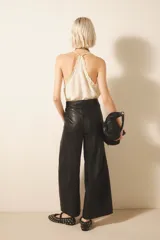 Pantalón de cuero ovino negro, de corte amplio con pierna ancha, pinzado y con acceso delantero de snaps metálicos y cierre. Incluye tiras regulables en la cintura y bolsillos laterales.