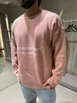 Sweater de punto color rosado con cuello redondo y diseño holgado. Presenta un estampado frontal con el texto 'Bohemian Dept' y 'Only Good News' en color blanco.