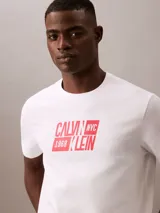 Remera blanca de algodón con cuello redondo y manga corta. Estampado frontal con el logo de Calvin Klein en rojo.