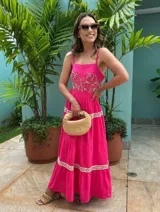 Vestido largo fucsia de lino con tirantes finos, escote recto y falda amplia en niveles con detalles de inserciones de encaje bordado en crudo en el pecho y los cortes de la falda.
