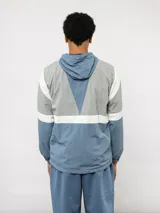 Campera de nylon Umbro con capucha, cierre frontal y diseño de bloques de color en gris, blanco y azul. Puños y dobladillo elásticos.