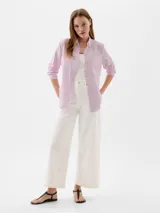 Camisa de corte clásico con cierre frontal de botones, cuello camisero, manga larga con puños abotonados y un bolsillo en el pecho con el logo de la marca bordado. Presenta un diseño de rayas verticales finas en tono rosado.