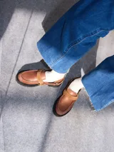 Mocasines color marrón de estilo urbano, confeccionados en cuero con plataforma de 4 cm. Presentan una tira con tachas pequeñas y argolla metálica en el empeine, y costuras pespunteadas alrededor de la puntera.