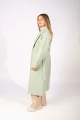Tapado de paño color verde claro, con solapas amplias, cierre frontal con un botón y lazo ajustable en la cintura.