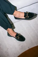 Mocasín de ecocuero negro con textura tipo croco, acabado brillante y detalle de herraje metálico dorado en el empeine.