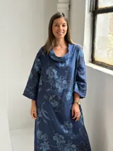 Vestido largo de lino azul marino con estampado floral en tonos más claros, de corte amplio, con cuello tipo cowl y mangas largas.