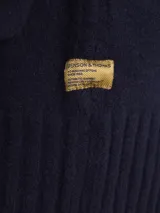 Cardigan de punto gris con cuello tipo chal y cierre frontal de botones. Presenta puños y ruedo acanalados, ofreciendo un diseño clásico y versátil.