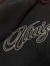 Hoodie negro con capucha y estampa gráfica blanca en la espalda con diseño tipográfico cursivo. Presenta puños y ruedo acanalados.