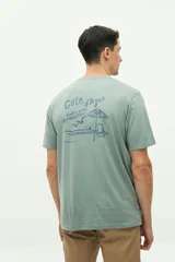 Remera de manga corta color verde agua con estampado gráfico en la espalda que incluye texto y motivos playeros. Confeccionada en algodón con calce regular.