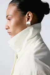 Trench oversize de cuello solapa y manga larga, con cintura ajustable mediante cordones y cierre frontal oculto. Cuenta con bolsillos laterales y forro interior.